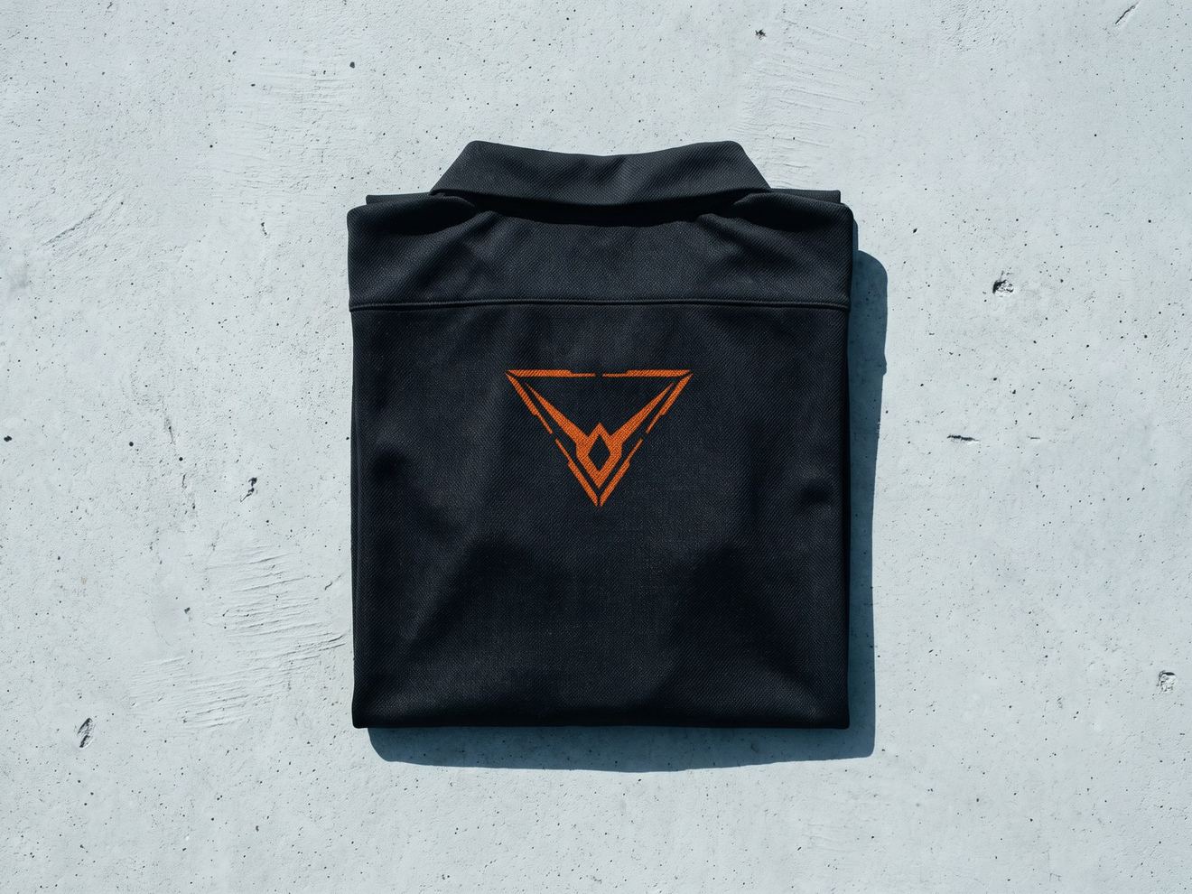 A render of a black training top folded square on concrete, the orange Hypereon mark on its chest