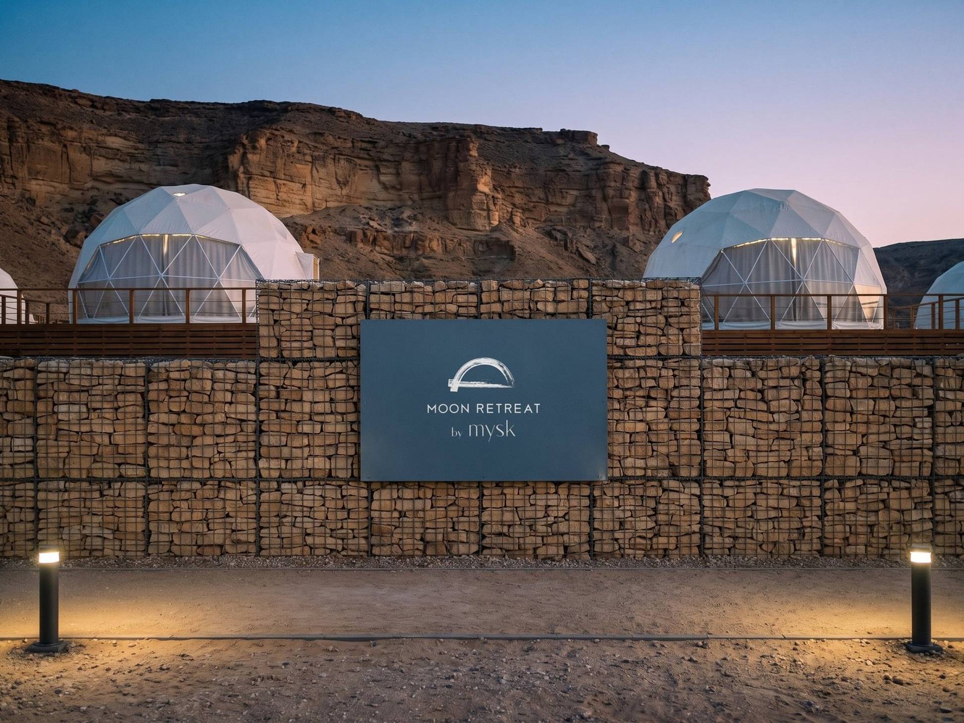A render of the Moon Retreat lockup on a slate panel in a stone wall, domes behind, at blue hour