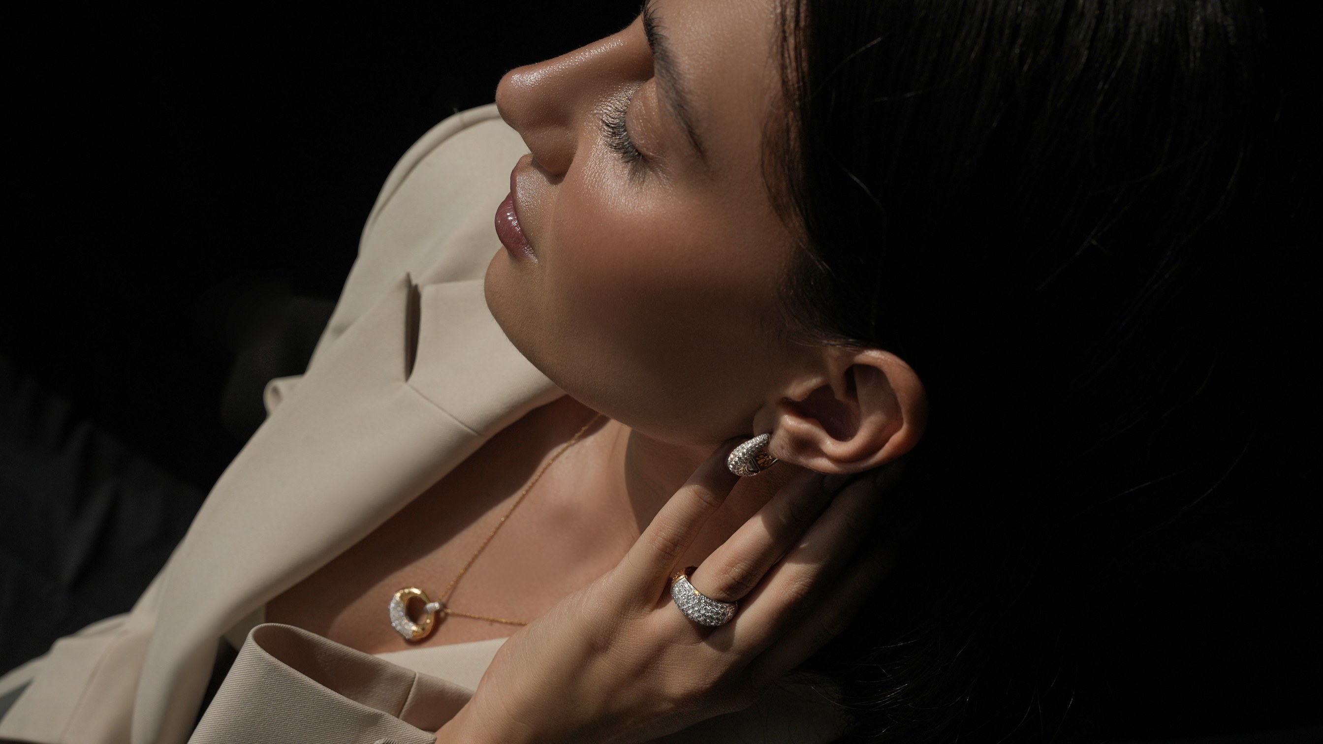 A woman with her head turned to the light, wearing the Sinan Pavé earring, ring and pendant